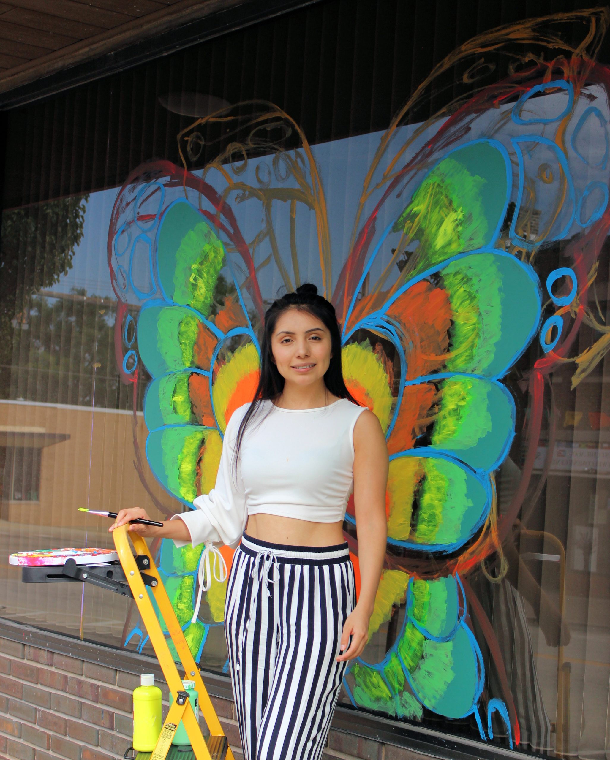 A local artist paints a window at Republic Bank on Main Street Saturday morning, the window art is a part of the decorations for the local WeGo Loteria sponsored by the Cultural Arts Commission in West Chicago